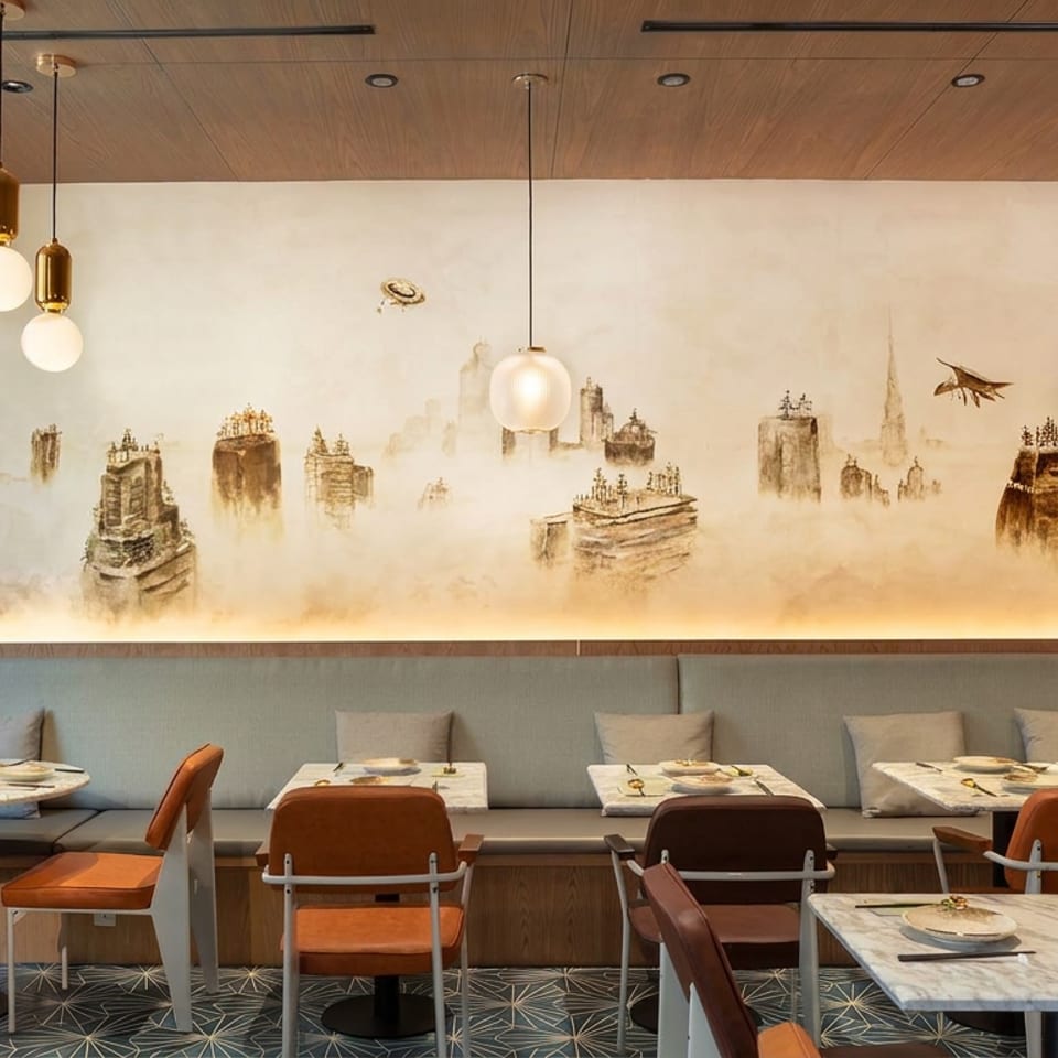 Contemporary restaurant dining room with set tables, pendant lights, banquette seating, and a misty cityscape mural.