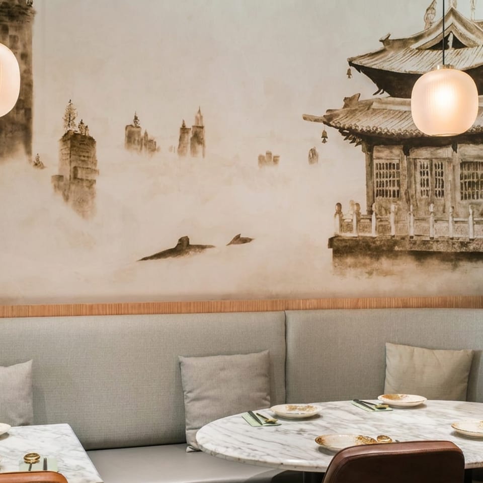 Elegant restaurant seating with marble tables, pendant lights, and a misty Asian pagoda mural.