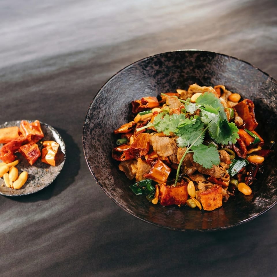 Spicy stir-fried dish with vegetables, peanuts, and cilantro in a black bowl, accompanied by chili pieces and peanuts.