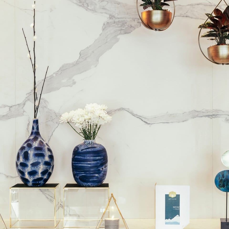 Elegant restaurant display with blue ceramic vases, white flowers, candles, hanging plants, and a marble wall.