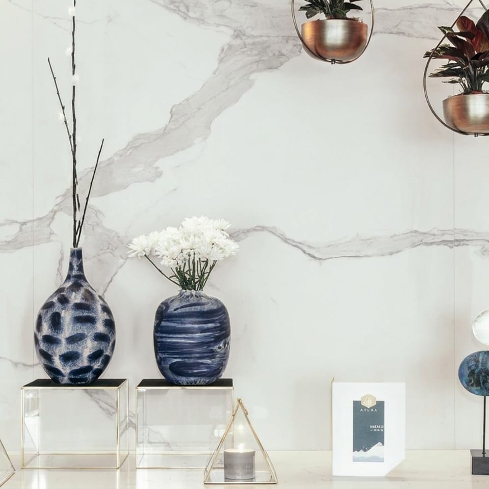 Elegant marble-paneled display featuring blue ceramic vases, white flowers, hanging plants, candles, and a restaurant menu.