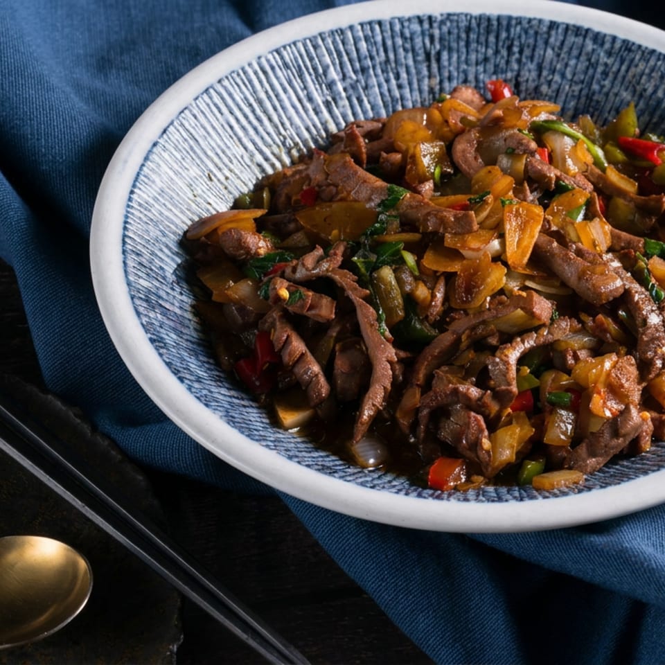 Bowl of stir-fried sliced meat and vegetables with peppers and onions, accompanied by chopsticks and a spoon on a blue napkin.